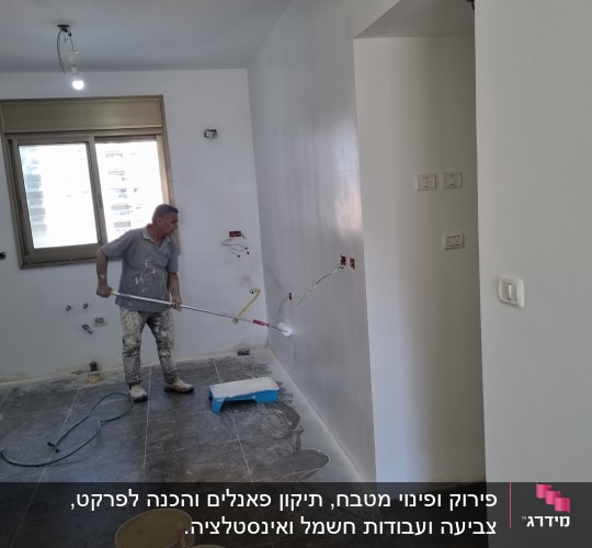 אדם צובע קיר עם רולר, דליים על הרצפה